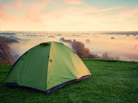Green tent on hill above misty riverの写真素材