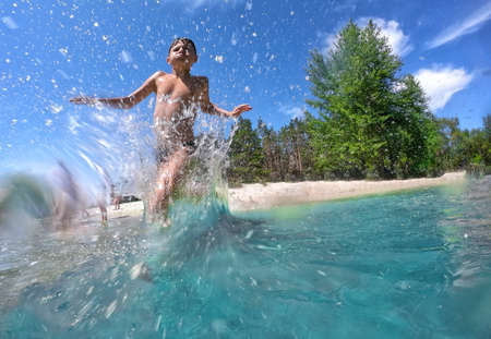 Boy runs into the water in the sprayの写真素材