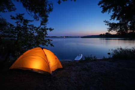 Illuminated from inside orange tent and surfboard on beachの写真素材