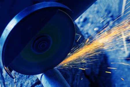 Sawing metal pipe with an electric saw. Sparks fly. Toning in blueの写真素材