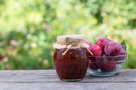 Jar of plum jam with plums on wooden tableの写真素材