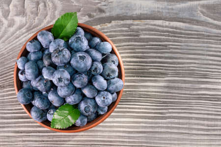 Blueberries with leaves in a brown clay bowl on a wooden background. View from aboveの写真素材