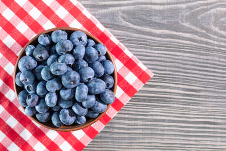 Blueberries in a clay bowl on a wooden table with a red checkered tablecloth. View from aboveの写真素材