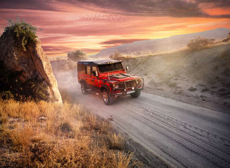 Red off-road car on a dusty road near the cliff. Dramatic sunset sky. Adventure and freedom travel conceptの写真素材