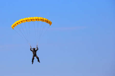 Skydiver with a yellow parachute in the blue sky. Trade marks and logos removed. Face hidden behind a helmet maskの写真素材