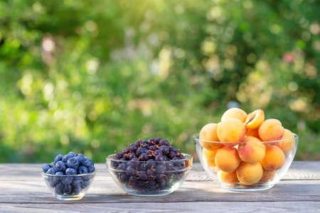 Apricot, currant and blueberry in bowls on wooden table. Green natural backgroundの写真素材