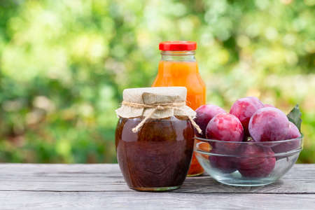 Plum jam and juice in jars and plums on a wooden table. Natural green backgroundの写真素材