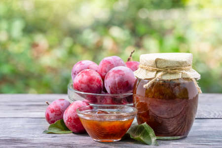 Plum jam in a jar and saucer and plums on a wooden table. Natural green background. Natural organic food conceptの写真素材