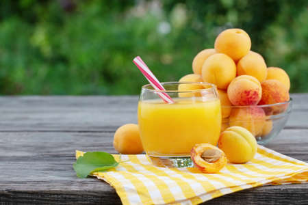Apricot juice in glass and apricots on wooden table. Checkered yellow napkin. Green natural backgroundの写真素材