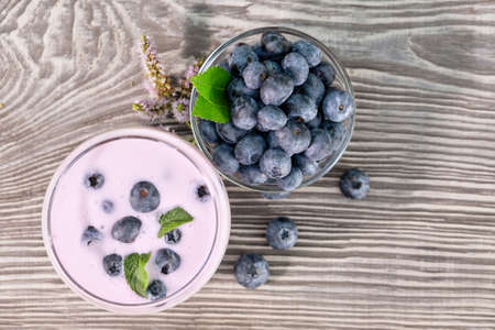 Berry smoothie or yogurt in a glass and blueberries in a bowl on a wooden table. Mint in a glass and on the table. The concept of detox. View from aboveの写真素材