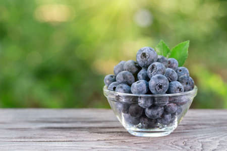 Blueberries with leaves in glass bowl on wooden tableの写真素材