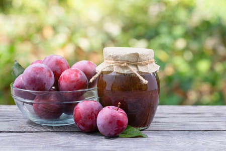 Plums in a transparent bowl and plum jam on wooden tableの写真素材