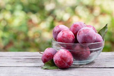 Plums in a transparent bowl on a wooden tableの写真素材