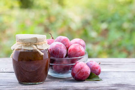 Plums in transparent bowl and jar of plum jamの写真素材
