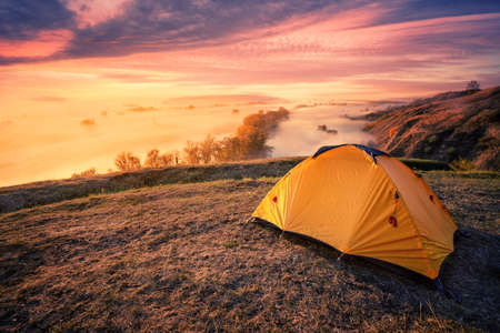Orange tourist tent on hill above foggy riverの写真素材