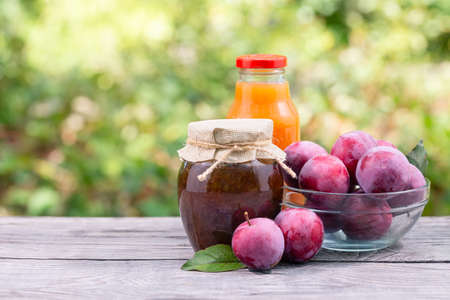Plum jam and juice in jars and plums on wooden tableの写真素材
