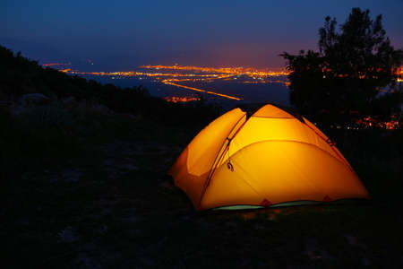 Orange lighted inside tent on mountain above city in night lightsの写真素材