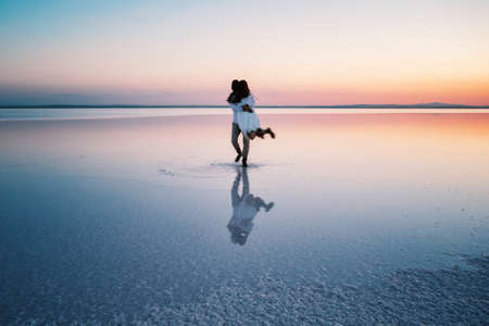 Silhouettes of hugging happy lovers in middle of shallow waterの写真素材