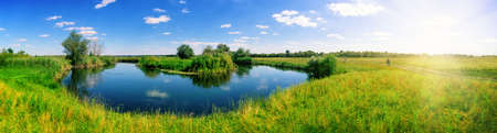 Turn of river in middle of meadow with green grassの写真素材