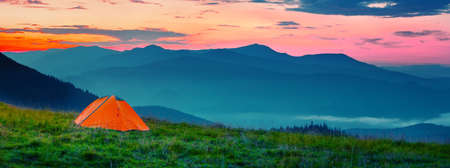 Orange tent in mountains at sunsetの写真素材