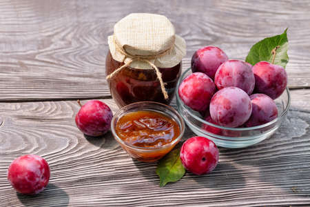 Plum jam in a closed jar and saucer and plums on a wooden table. View from aboveの写真素材