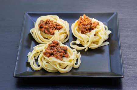 Spaghetti with meat laid out on a black square plate. Black background. Traditional italian dishの写真素材
