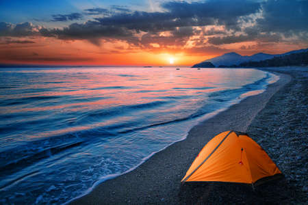 Orange tent by the sea or ocean on a background of mountains. Dramatic sunset skyの写真素材