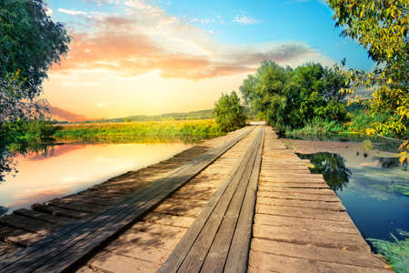 Wooden bridge or pier on the lake. Dramatic sunset sky. Summer landscapeの写真素材