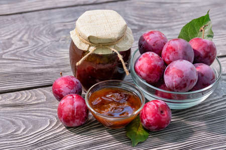 Plum jam in jar and saucer and plums on wooden tableの写真素材