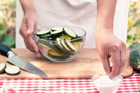 Female hands salt sliced zucchini on a wooden board