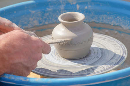 Potter's hands put a pattern on a jug on a potter's wheelの写真素材