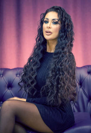 Young beautiful girl with long curly dark hair on leather sofa