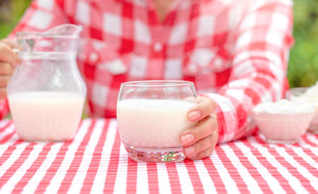 A girl in a red plaid shirt holds out a glass of milkの写真素材