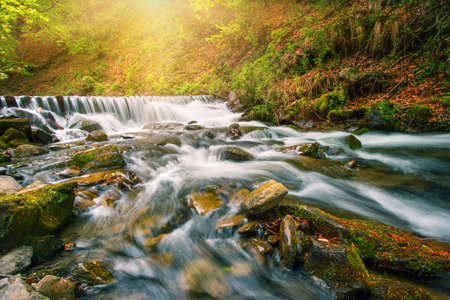 Waterfall on a mountain river in the autumn forest under bright sunの写真素材