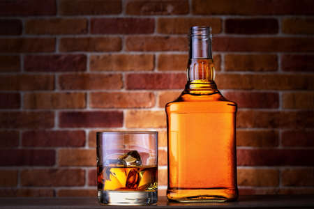 Glass of whiskey with ice and a bottle on a brick wall backgroundの写真素材