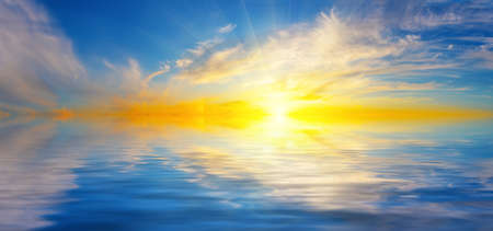 Panorama of evening dramatic sky with bright sun over sea surfaceの写真素材