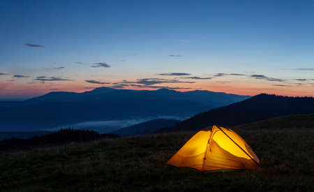 Orange luminous tent on the mountain in evening or early morningの写真素材