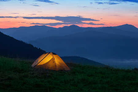 Orange tourist tent illuminated from inside on mountain