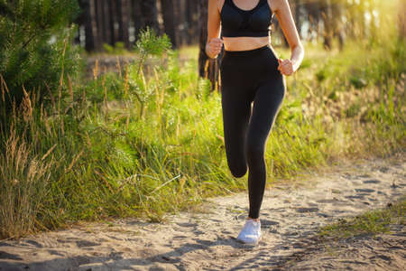Legs of running girl sportswoman on road in forestの写真素材