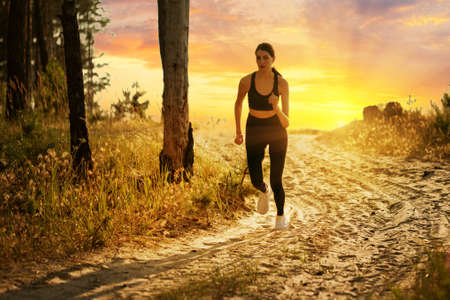 Silhouette of girl running on forest road at sunsetの写真素材