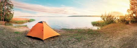 Orange tourist tent on sandy shore of lake at sunriseの写真素材