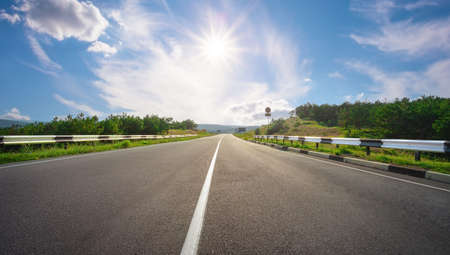 Asphalt highway with backlit sun on blue skyの写真素材