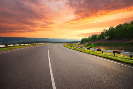 Curving asphalt road under dramatic sunset skyの写真素材