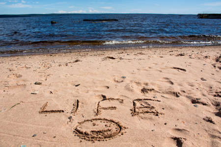 The inscription on the shore of the lake in the sand, against the blue sky and water.の写真素材