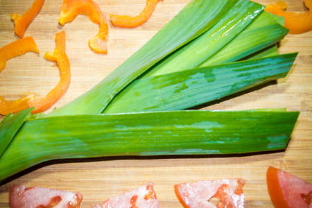 Onions, peppers and tomatoes for cooking salad on a wooden board backgroundの写真素材