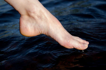 The foot touches the water surface on the lake shoreの写真素材