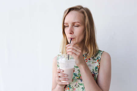A beautiful and young girl standing on a white background. She is very joyful and enjoys the drink. The drink is so delicious. Her enjoyment is not a measure.の写真素材