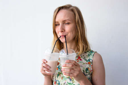 A beautiful and young girl standing on a white background. She is very joyful and enjoys the drink. The drink is so delicious that she drinks it with two glasses. Her enjoyment is notの写真素材