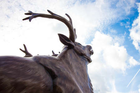 A large deer is made of wood against the sky. The deer has large horns that, against the sky, seem to touch the clouds. The head of a deer is raised to the sky.の写真素材