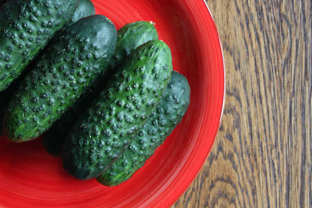 A few cucumbers on a red plate. The plate is made of clay and stands on a wooden surface. Cucumbers are fresh and ready to eat.の写真素材